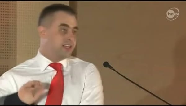 Młody Krzysztof Gawkowski w białej koszuli i w czerwonym krawacie podwija rękawy.